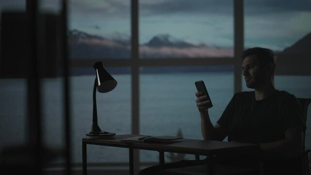 Silhouette of a man sitting at a table looking at a mobile phone thinking and analyzing the stock market, solving personal problems, repayment of loans, Internet banking