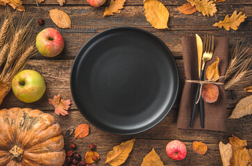 Thanksgiving day background with a black plate, cutlery, pumpkin, apples and autumn leaves. Top...