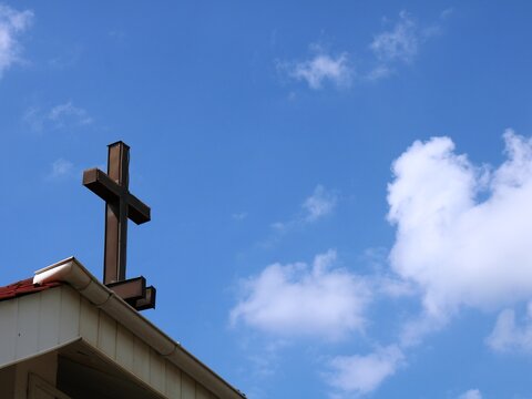 discreet Christian crucifixion on the corner of the roof of the church against the background of deep nea with light clouds, conceptual image of the Protestant cross on the building going to heaven