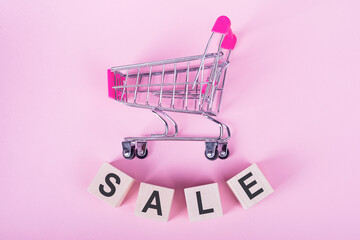 SALE - word on wooden cubes, on a pink background with a shopping trolley.