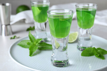 Fototapeta premium Delicious mint liqueur with lime and green leaves on white table, closeup
