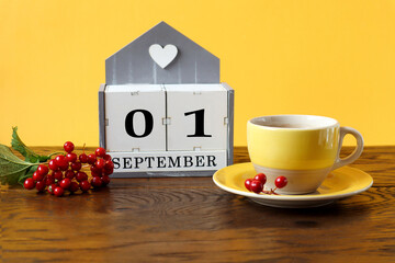 Calendar for September 1 : the name of the month in English, cubes with the numbers 0 and 1, a yellow cup of tea on a saucer, a branch of viburnum on a wooden table, a yellow background, side view