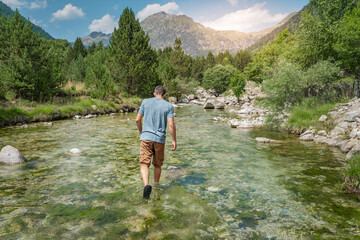 Young man walking inside the river in a beautiful  landscape during the sunset. Natural and wild lifestyle Relax, disconnection and freedom concept. Travel and vacations concept.