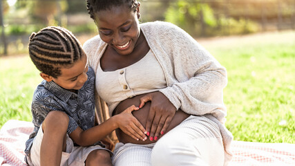 Happy African family expecting other baby - Afro Mother and son touching pregnant belly doing heart shape with hands - Parents love and maternity lifestyle concept - 453436898