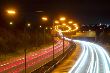 Fototapeta na wymiar Motorway, freeway or highway at night with orange sodium street lighting. M60, England, UK. Light trails, busy, commute
