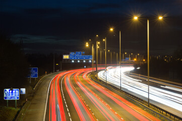 Smart motorway in England, UK with light trails signifying busy traffic at rush hour. The banner...