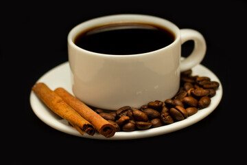 A cup of hot coffee in a white coffee cup. A cup on a saucer with roasted coffee beans and cinnamon sticks.