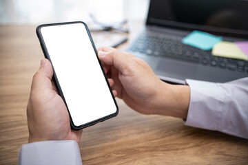 Close up white display of smartphone in hand business man and laptop computer with wood table in background