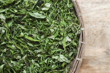 Dry green leaves of andrographis paniculata or kariyat tree (fah talai jone) in bamboo threshing basket, Thai traditional herb and has antipyretic properties close-up.