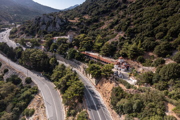 a panoramic view of the white stone church against the backdrop of mountains and olive groves of Crete filmed from a drone 