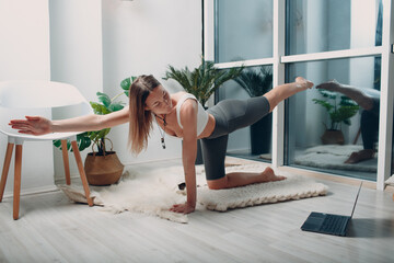 Adult woman doing yoga at home living room with online tutorials on laptop