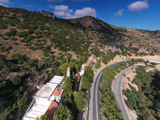 a panoramic view of the white stone church against the backdrop of mountains and olive groves of Crete filmed from a drone 