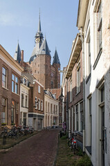 Zwolle, The Netherlands, August 9, 2021: Narrow street in the old town with the tower of Sassenpoort gate rising above the brick and plaster facades.