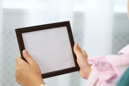 Little girl holding empty photo frame indoors, closeup