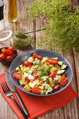 Italian pasta fusilli tricolore with cherry tomatoes, zucchini and feta cheese in a blue shallow bowl on a red napkin with black silverware on a wooden surface