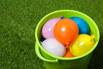 Bucket full of colorful water bombs on green grass, closeup. Space for text
