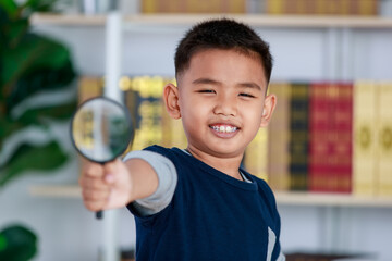 Circle magnifying glass tightly grab by genius Asian boy for studying funny knowledge of scientific...