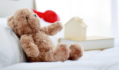 Brown lovely fluffy teddy bear toy sitting alone on bed in bedroom
