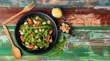 Rocket salad with tomato, crouton, herb roasted chicken in black dish together with wooden utensil...