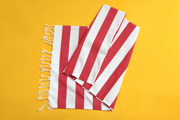 Folded striped beach towel on yellow background, top view