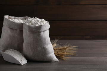 Sacks with flour and wheat spikes on wooden background. Space for text