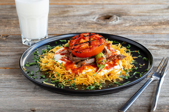 Turkish Cokertme Kebab on a wooden floor. Cokertme kebab is made with grated french fries, yoghurt, tomato sauce and cooked beef.