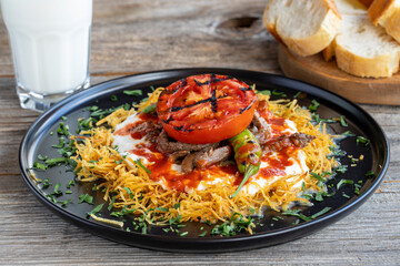 Turkish Cokertme Kebab on a wooden floor. Cokertme kebab is made with grated french fries, yoghurt, tomato sauce and cooked beef.