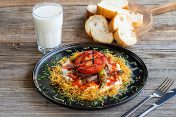 Turkish Cokertme Kebab on a wooden floor. Cokertme kebab is made with grated french fries, yoghurt, tomato sauce and cooked beef.