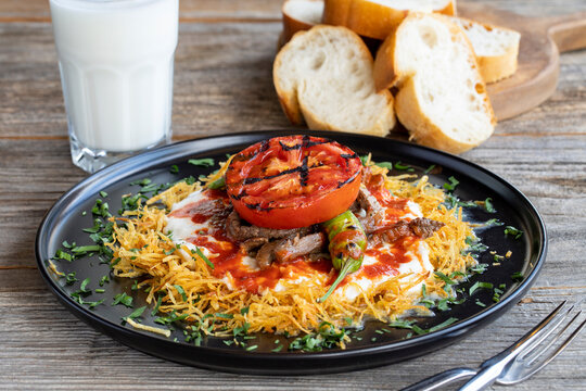 Turkish Cokertme Kebab on a wooden floor. Cokertme kebab is made with grated french fries, yoghurt, tomato sauce and cooked beef.