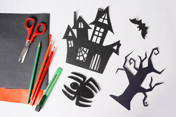 The child create Halloween paper decor tree, spider and house. scissors on white table. Craft for kids.