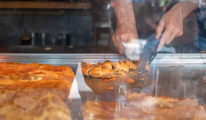 Man cutting bougatsa in small pieces in a shop display. Traditional pastry with minced meat, street food.