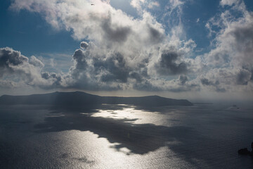 ギリシャ　サントリーニ島のフィラから見える太陽に雲がかかって影の出来たエーゲ海とティラシア島