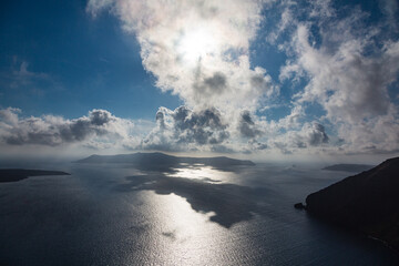 ギリシャ　サントリーニ島のフィラから見える太陽に雲がかかって影の出来たエーゲ海とティラシア島