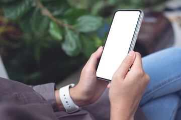 Mockup image of hand holding white mobile phone with blank black screen on thigh
