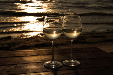Two glasses of wine on wooden table near river at sunset