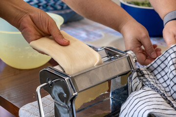 Fresh pasta homemade preparation. Hands working in the kitchen, pasta maker machine closeup view