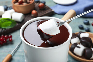 Dipping marshmallow into melted chocolate at blue wooden table, closeup