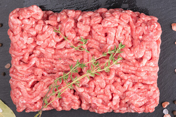 Close-up of minced meat with sprigs of cumin on a stone slate board.