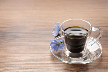 Glass cup of delicious chicory drink and flowers on wooden table, space for text