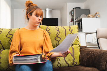 Caucasian female sitting on a couch looking at a document and holding a folder
