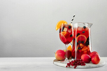 Glass and jug of Red Sangria on white wooden table against light grey background. Space for text