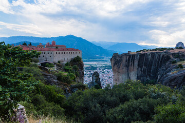 Fototapeta na wymiar ギリシャ　メテオラの断崖絶壁の岩山の上に建つ聖ステファノス修道院と奇岩群の隙間から覗くカランバカの街並みと後ろに広がるピンドス山脈