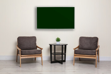 Modern wide screen TV on white wall in room with stylish furniture