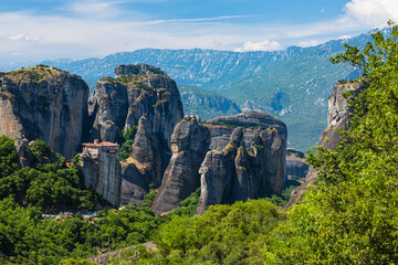 Fototapeta na wymiar ギリシャ　メテオラの断崖絶壁の岩山の上に建つルサヌ修道院と周りを囲む奇岩群と後ろに広がるピンドス山脈