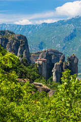 Fototapeta na wymiar ギリシャ　メテオラの断崖絶壁の岩山の上に建つルサヌ修道院と周りを囲む奇岩群と後ろに広がるピンドス山脈