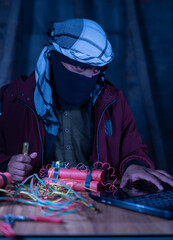 Terrorist with face cover learning timer bomb making looking into laptop.