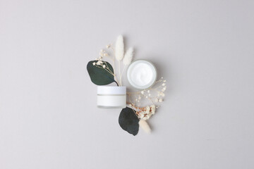 Jars of cosmetic cream with eucalyptus and flower on grey background. Flat lay, copy space