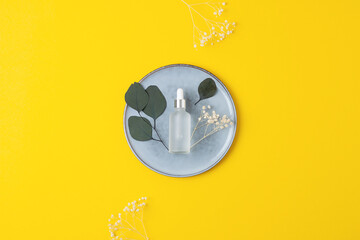 Cosmetic bottle with eucalyptus and plate on yellow background. Flat lay, copy space