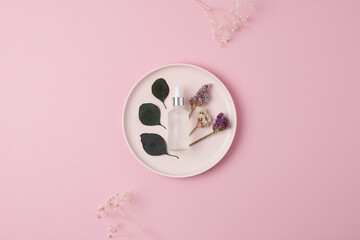 Cosmetic bottle with eucalyptus and plate on pink background. Flat lay, copy space