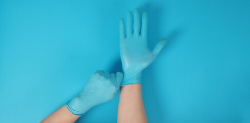 Hand is pulling blue latex gloves on blue background.